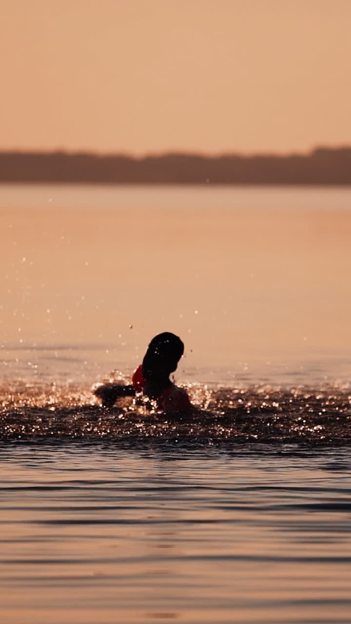 Silhouette of boy at sunset in the river. Silhouette of a child playing splash water in river Vertical video
