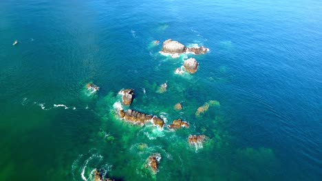 Overhead-Flight-for-Rocks,-Reefs-and-Waves-Crashing-in-Clear-Blue-Water