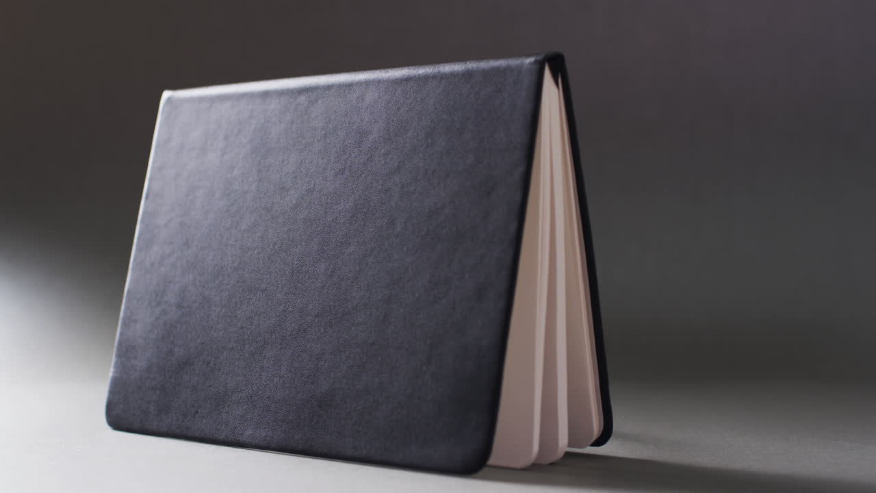 Close up of open black book standing horizontal with copy space on gray background in slow motion