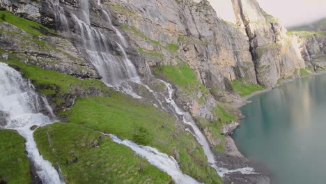 aerial flight next to a beautiful big waterfall on a mountain landscape, drone flying over a blue lake - oeschinen lake, switzerland