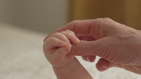 close up baby hand holding mother thumb, massaging, cuddling in bright bedroom