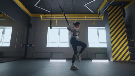 doing trx exercises. young athletic woman in sports clothing training legs with trx fitness straps in the gym. exercise where stabilizing muscles trained and the whole body is working truly functional