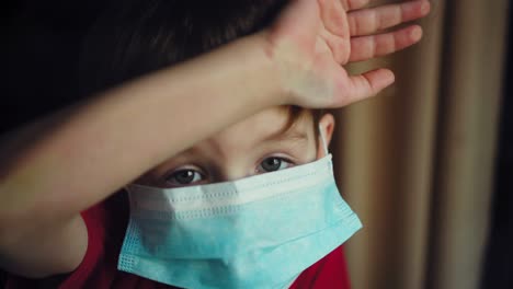 un niño con una máscara médica mira por la ventana 05