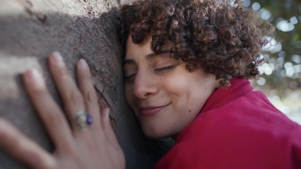 Primo piano di una donna serena che appoggia la testa contro il tronco di un albero