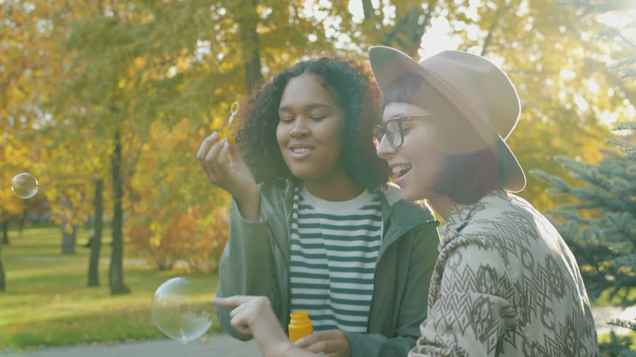 Two friends enjoying the autumn park, blowing bubbles