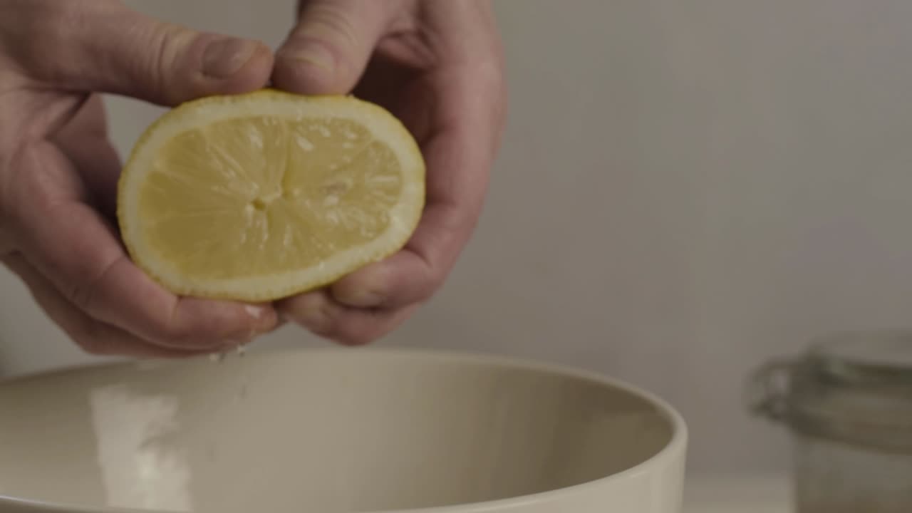 Hand squeezing juicy lemon into a bowl medium shot