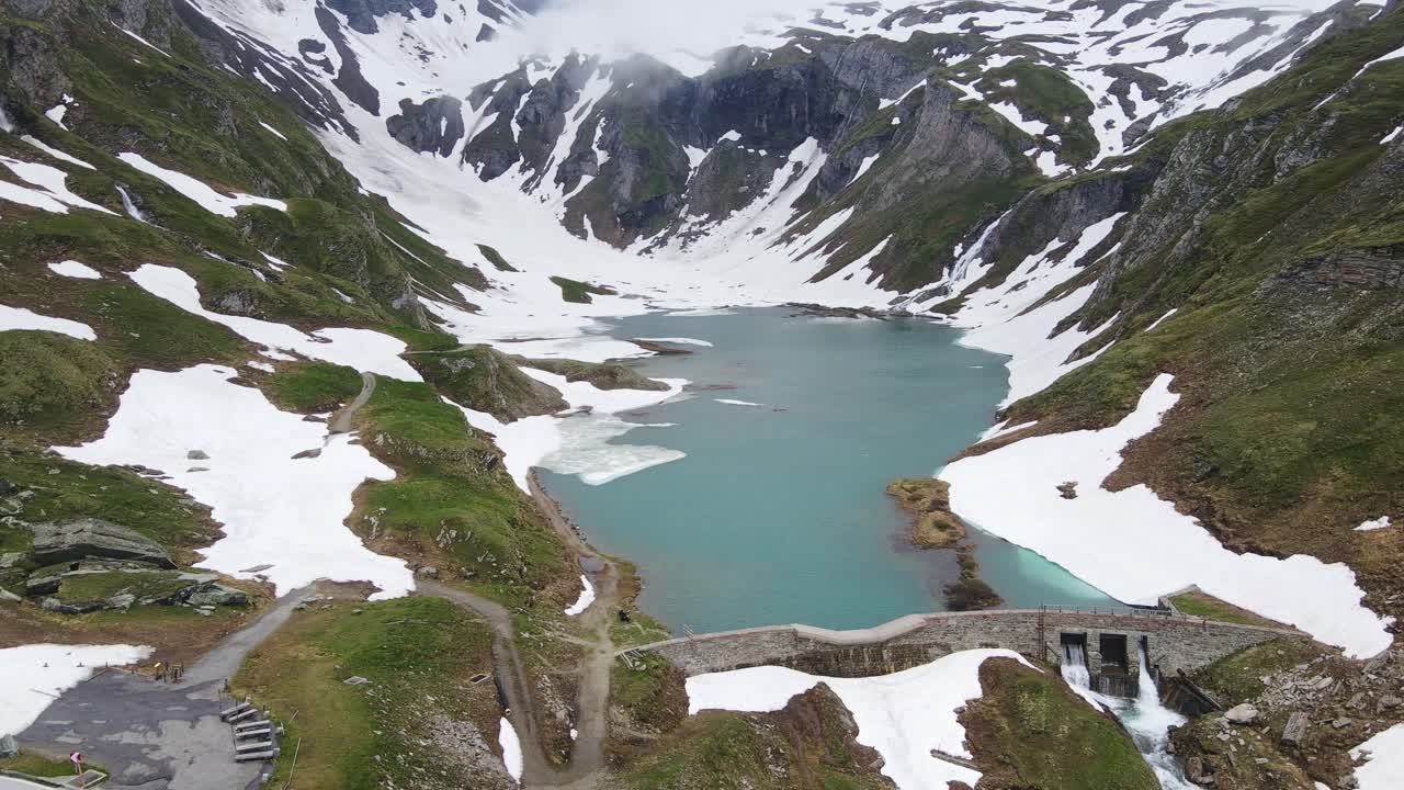 Cinematic pull-away shot, Naßfeld reservoir with Austrian alpine peaks and snow