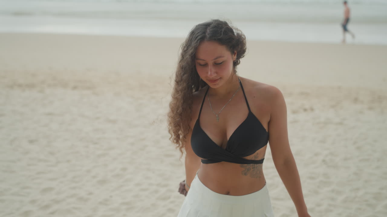 Passeggiata in bikini su una spiaggia dell'isola, un passo casuale sulla sabbia sotto un cielo tenue, movimenti spontanei e una leggera brezza che incorniciano la scena come una sessione fotografica, una viaggiatrice dell'isola, una ballerina da spiaggia e una cercatrice di tramonti che esplora.