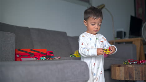 slow motion of a young toddler wearing pajamas playing with a yellow car toy on the couch