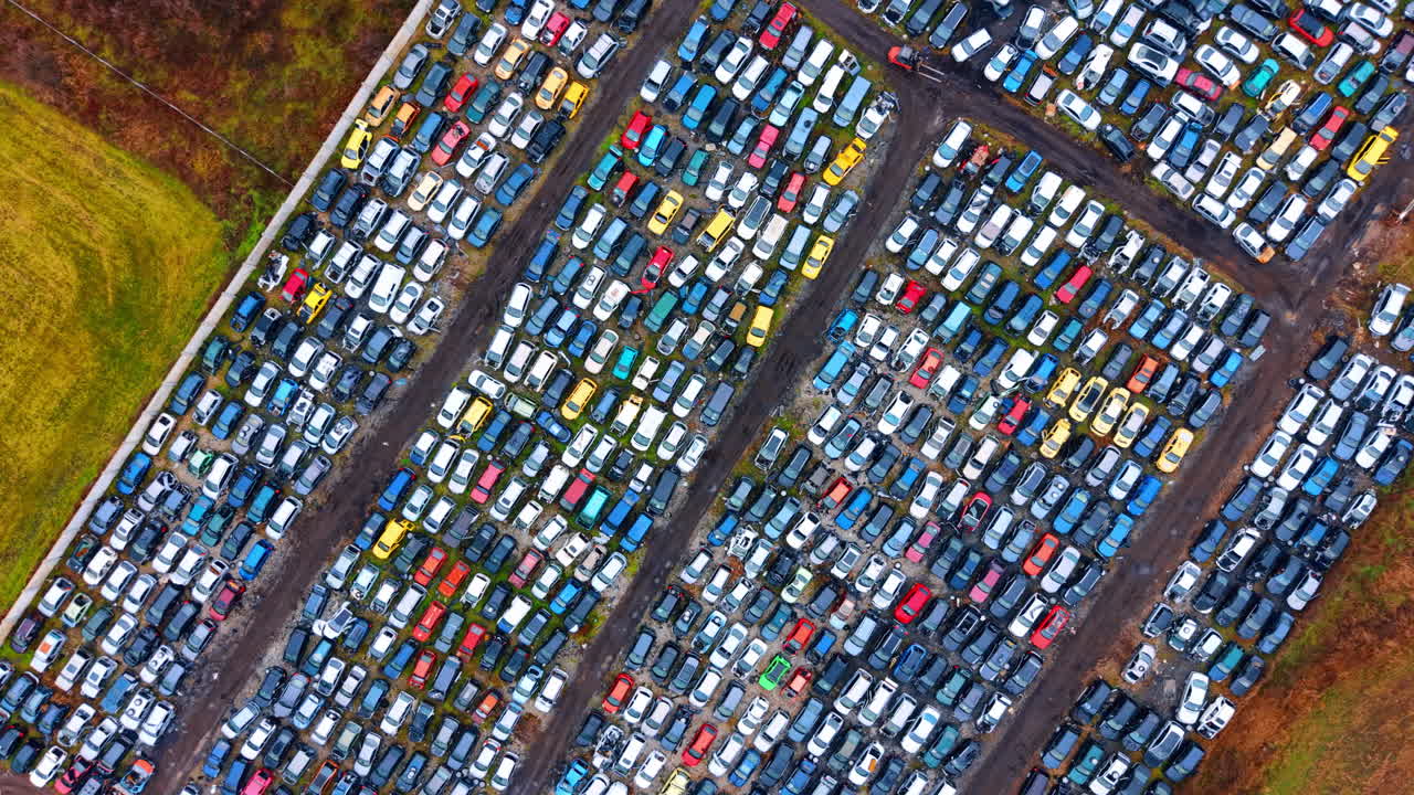 Expansive aerial view of organized auto salvage yard. Wide top down shot of thousands of scrapped cars arranged in neat rows separated by dark ground paths