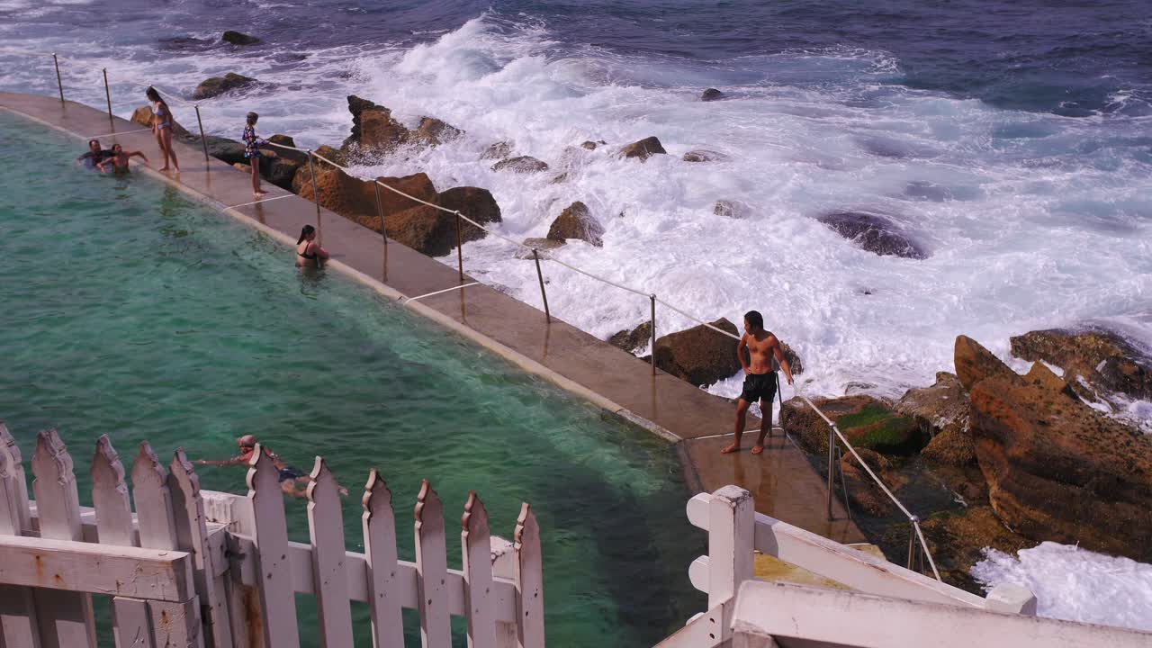 la hermosa playa bronte en australia con una piscina con vistas a las olas rompiendo y salpicando en grandes rocas junto a la orilla - cámara lenta
