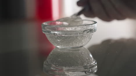 face mask gel bubbles shimmering on glass surface with expert gloved hand dipping brush into small bowl creating reflective skincare prep scene under soft ambient light for beauty treatment setup