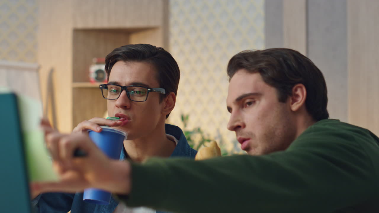 Focused designers pointing display eating food cabinet closeup. Guys lunch break