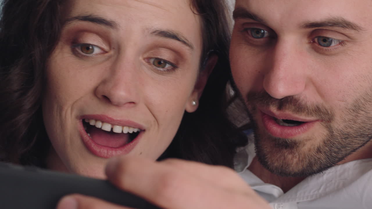 행복한 커플이 스마트폰을 이용해 비디오 채팅을 하고 친구와 채팅을 하고 놀란 모습을 하고 휴대폰으로 온라인 커뮤니케이션을 즐기고 있습니다.