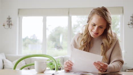 glimlachende vrouw die thuis aan tafel zit en de huishoudelijke financiën beoordeelt open brief met goed nieuws