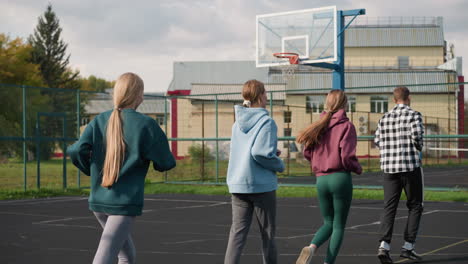 young sports enthusiasts running in sports court, with coach visible in background, all dressed in sportswear, focus on their movement as they participate in physical training session outdoors