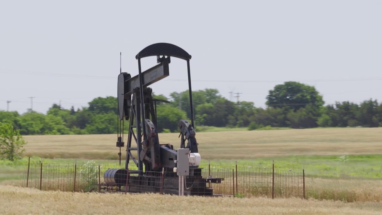 Drone 4K of a wheat field with two oil pump jacks and wind turbines in the background.