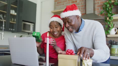 Happy-african-american-senior-couple-in-santa-hats-on-video-call-on-laptop-at-christmas-time