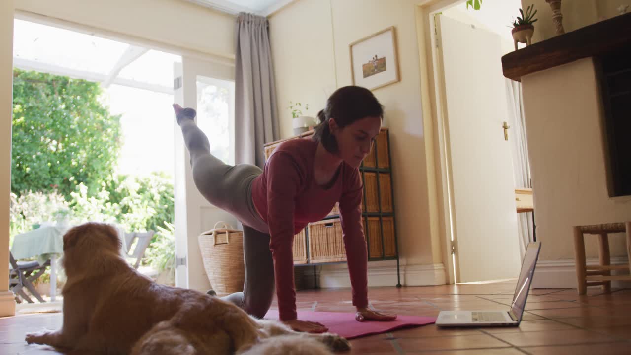 Caucasian woman exercising with her pet dog using laptop at home