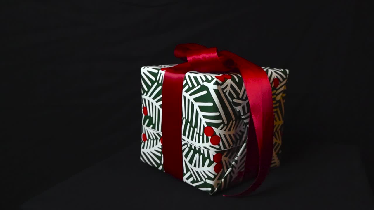 кадр изображает красиво упакованный подарок на фоне студии, рождественскую тему в 4k. подарок с яркой красной лентой. милая подарочная коробка помещена на черном фоне, придавая дух праздничного сезона