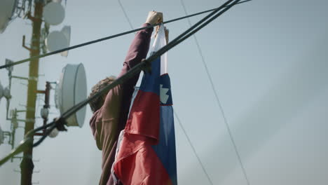 un joven está atando una bandera eslovena en un cable cerca de una torre de radio en la montaña mrzlica