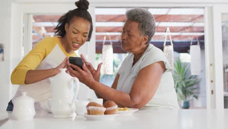 African-american-mother-and-daughter-smiling-while-using-smartphone-together-at-home
