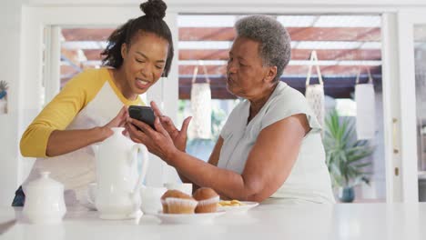 Afroamerikanische-Mutter-Und-Tochter-Lächeln,-Während-Sie-Zu-Hause-Gemeinsam-Das-Smartphone-Nutzen