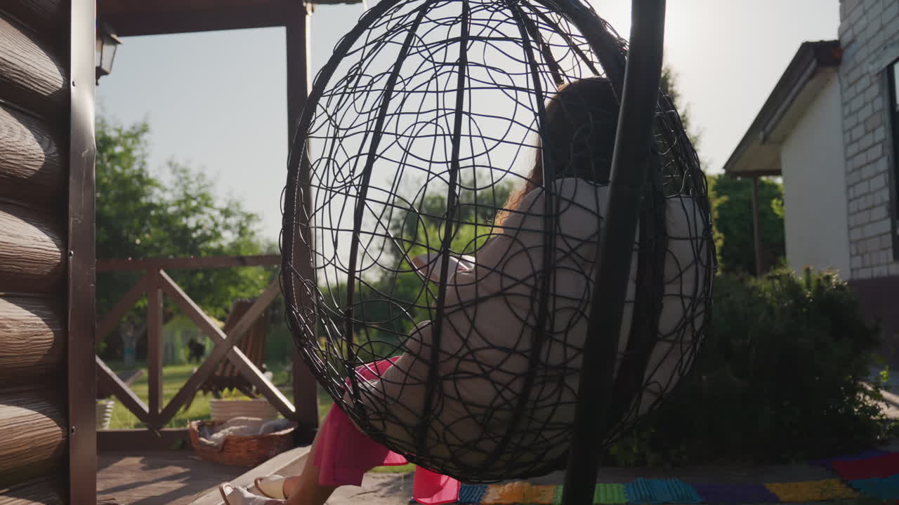 Woman Leaning Back On Sunny Porch Swing, Caucasian Woman Leisurely Reclining In Vibrant Garden Setting, Female Enjoying Calm Moment On Outdoor Swing Beneath Clear Sunlight In Garden