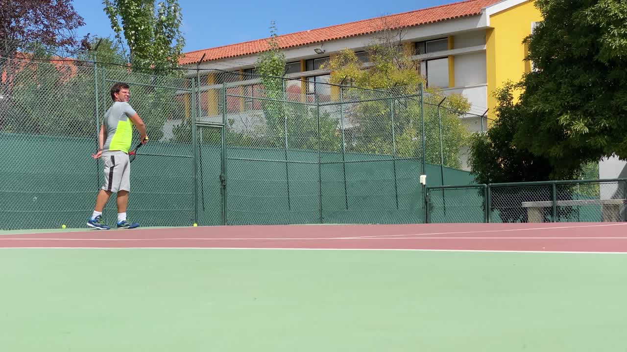 un joven en forma con ropa deportiva jugando al tenis en una cancha dura en un día soleado