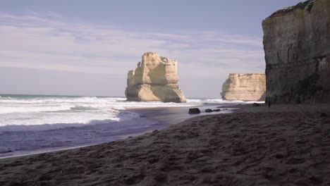 Waves-gently-breaking-on-the-shore-with-rock-formations-in-the-background,-Great-Ocean-Road,-Victoria,-Australia