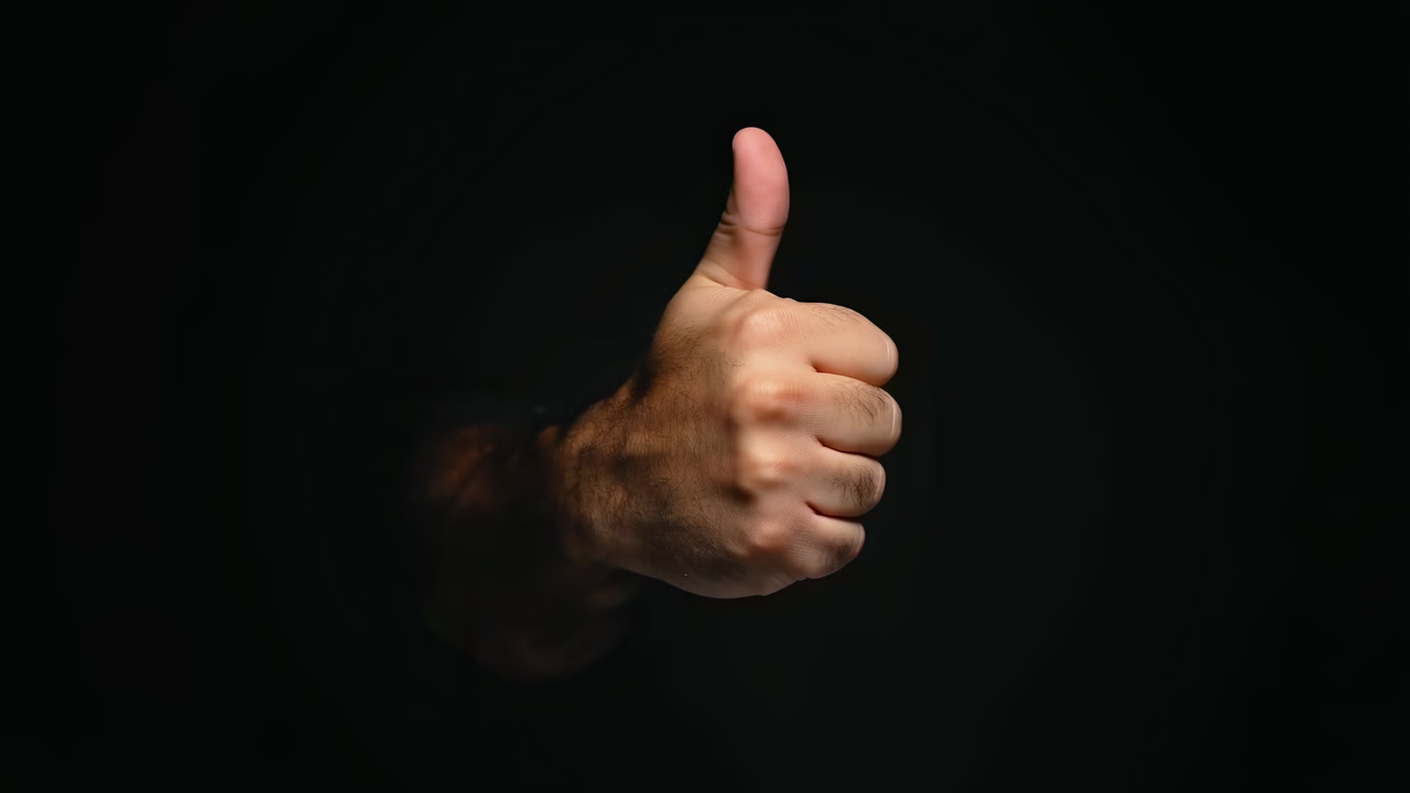 Closeup Hand Giving Thumbs Up Approval In Dark Studio Setting, Masculine Forearm Emerges From Black