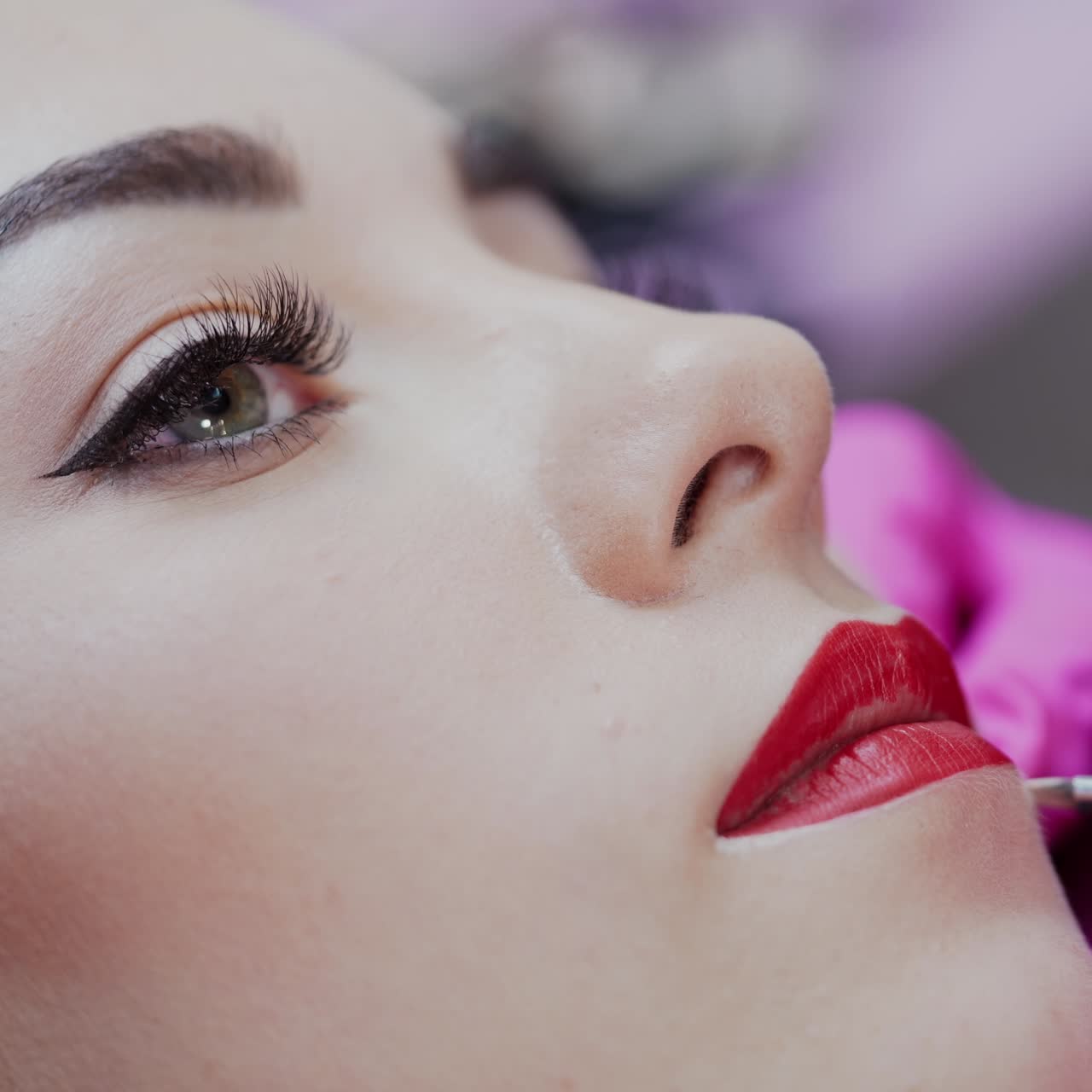 Cosmetic artist applying permanent makeup on lips. Cosmetology procedure. Professional tattooist making permanent make up to a girl. Close-up.