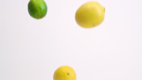 whole lemons and limes falling in slow motion on white backdrop and bouncing around