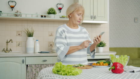 senior woman cooking salad with smartphone