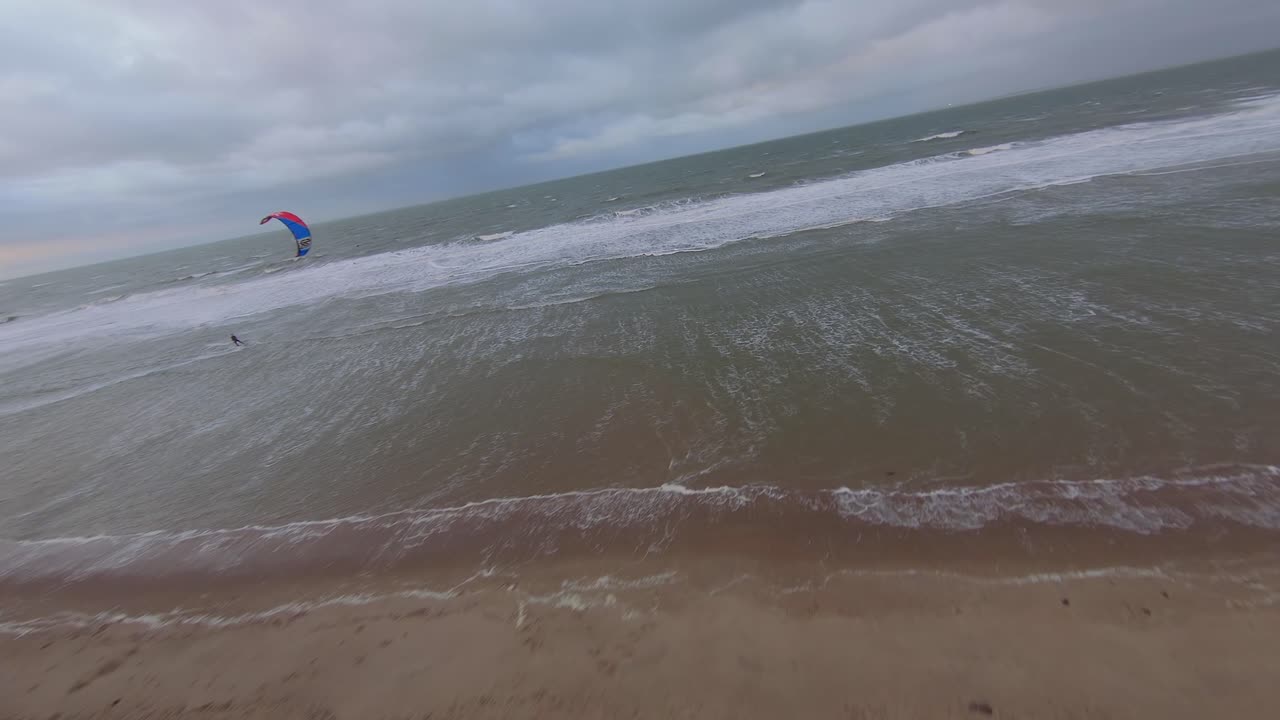 toma de órbita aérea amplia de una playa holandesa con un kitesurfista