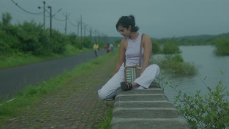 slow motion shot of an attractive young indian woman gracefully takes a seat by the tranquil river