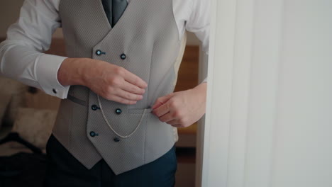 Groom-adjusting-pocket-watch-in-vest-pocket,-preparing-for-wedding-with-elegant-attire