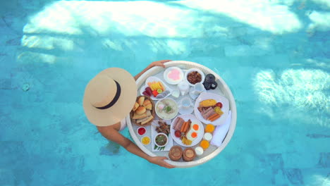 top down shot of woman walking with breakfast basket in swimming pool