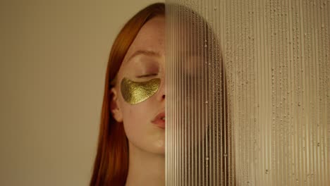 woman with gold eye patches behind a glass panel