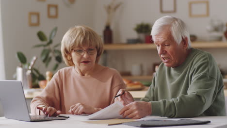 senior couple going through papers and using laptop at home