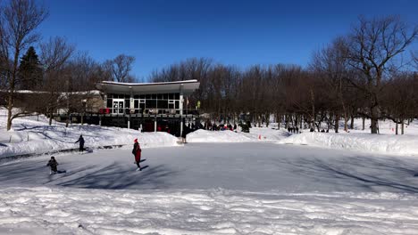 Ice-skaters-practicing-their-maneuvers-as-they-glide-on-the-ice-outdoors-in-front-of-a-building-with-snow-covering-the-perimeter-of-the-rink