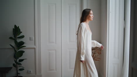 relaxed woman looking window morning indoors. tender girl peeping from curtain