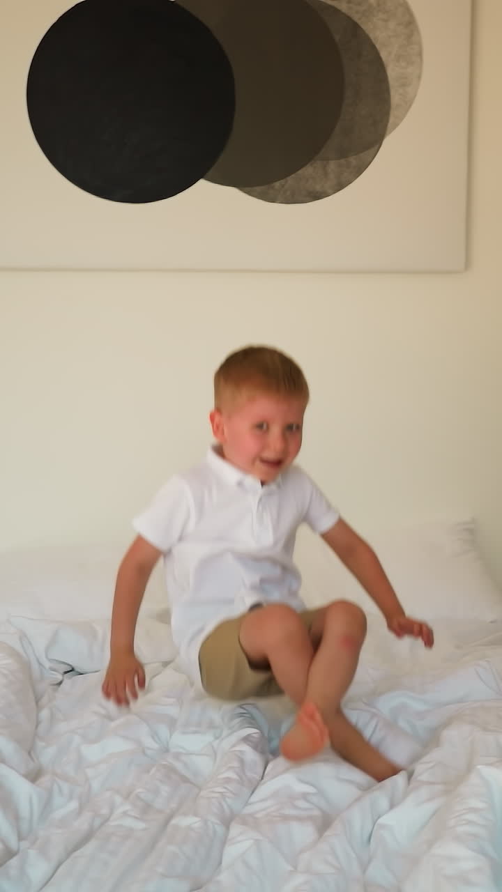 사랑스러운 유아는 편안한 침대에 뛰어다니며 재미를 느니다. 금발 아이는 밝은 방에서 놀면서 기을 발산합니다. 흥미진진한 순간으로 가득 찬 행복한 어린 시절 기억