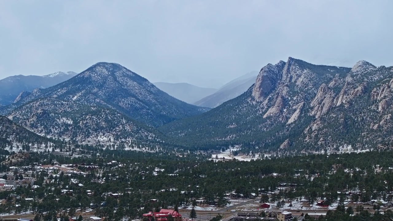 Città di Estes Park con foreste e Montagne Rocciose coperte di neve sotto un cielo nuvoloso, panoramica aerea con drone.