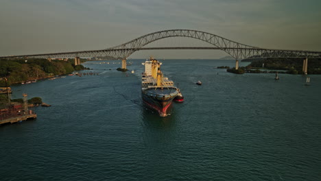 panama city aerial v52 cinematic reverse flyover the water canal capturing cargo carrier ship with bridge of americas in the background at sunset golden hours - shot with mavic 3 cine - march 2022