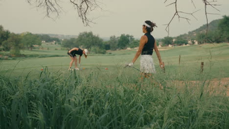 two lady golfers on the tee box preparing to start their round. one places her tee in the ground while her female partner walks up. outdoor golf course scene on a sunny day in slow motion