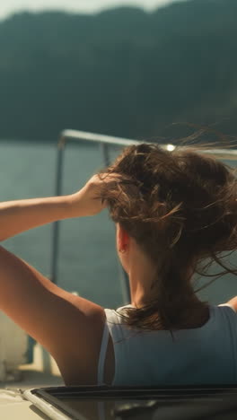 woman with hair disheveled from wind looks out of open hatch of cabin on motorboat sailing on lake. relaxation and scenic view in warm weather