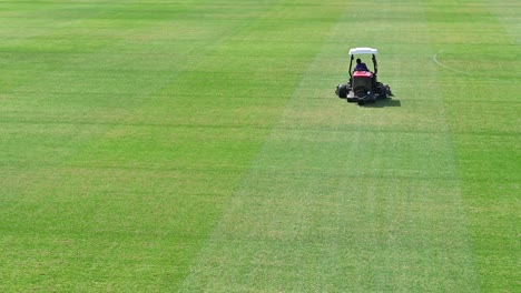 imágenes de 4k: un personal en un vehículo para cortar césped prepara un campo deportivo en un día soleado de verano en dubai, emiratos árabes unidos