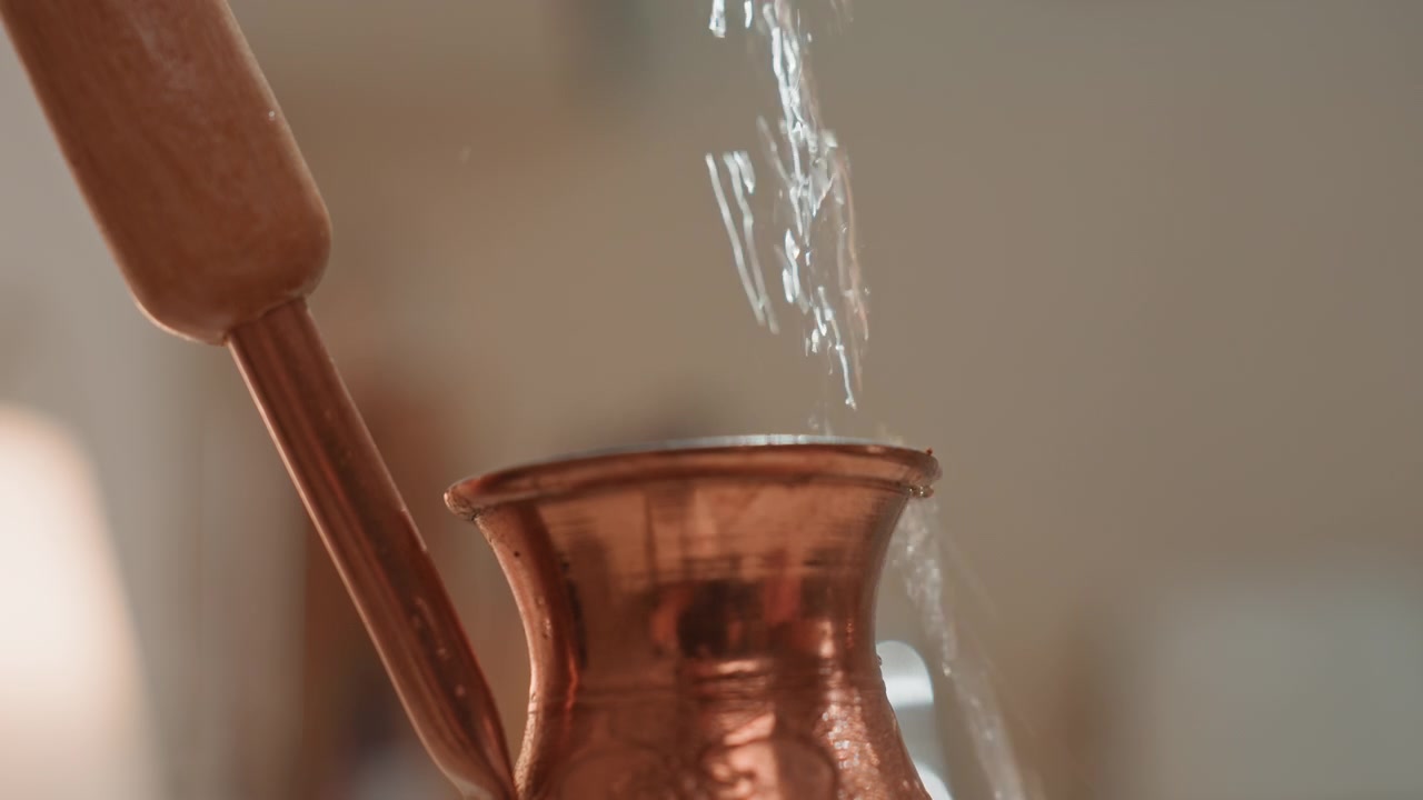 Schizzo d'acqua dinamico in una cezve di rame, goccioline cinetiche e bagliori luminosi, macro primo piano che cattura ritmo e tempo, momento giocoso del barista con movimento ritmico ed energica energia musicale