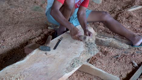 poor carpenter sculpting timber piece with chisel and hammer sits on shavings